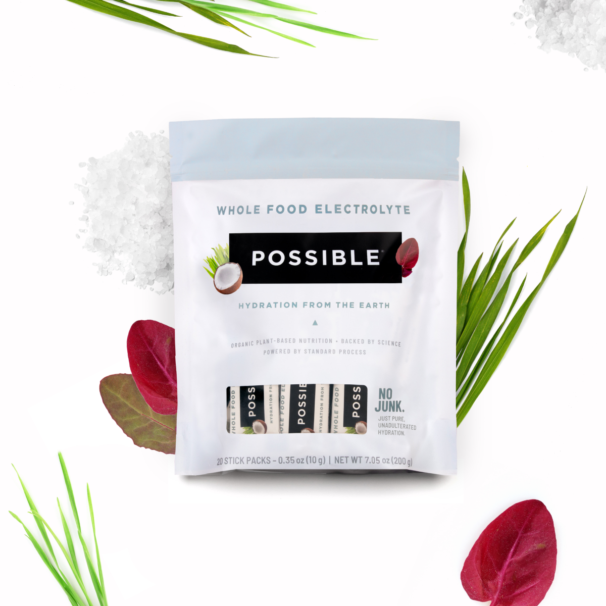 Image of a Possible Whole Food Electrolyte powder pouch with a white and light gray design, surrounded by fresh green leaves and red vegetable slices on a white background. The image highlights natural ingredients and hydration benefits.